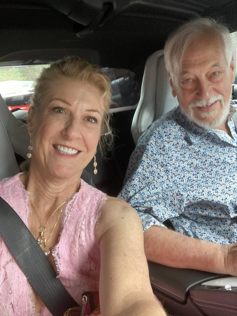 Evans Harrell and his wife Mo Burke, smiling in a car on a sunny day