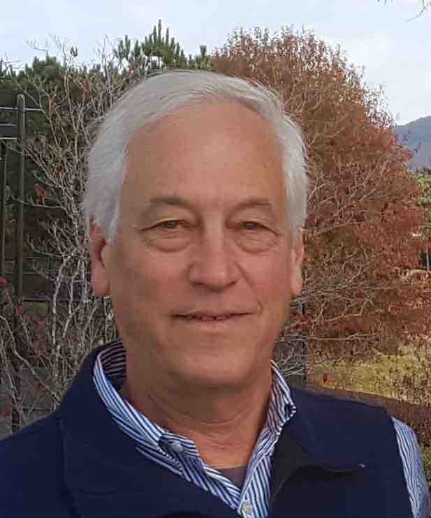 Evans Harrell, smiling, outdoors in front of autumn foliage