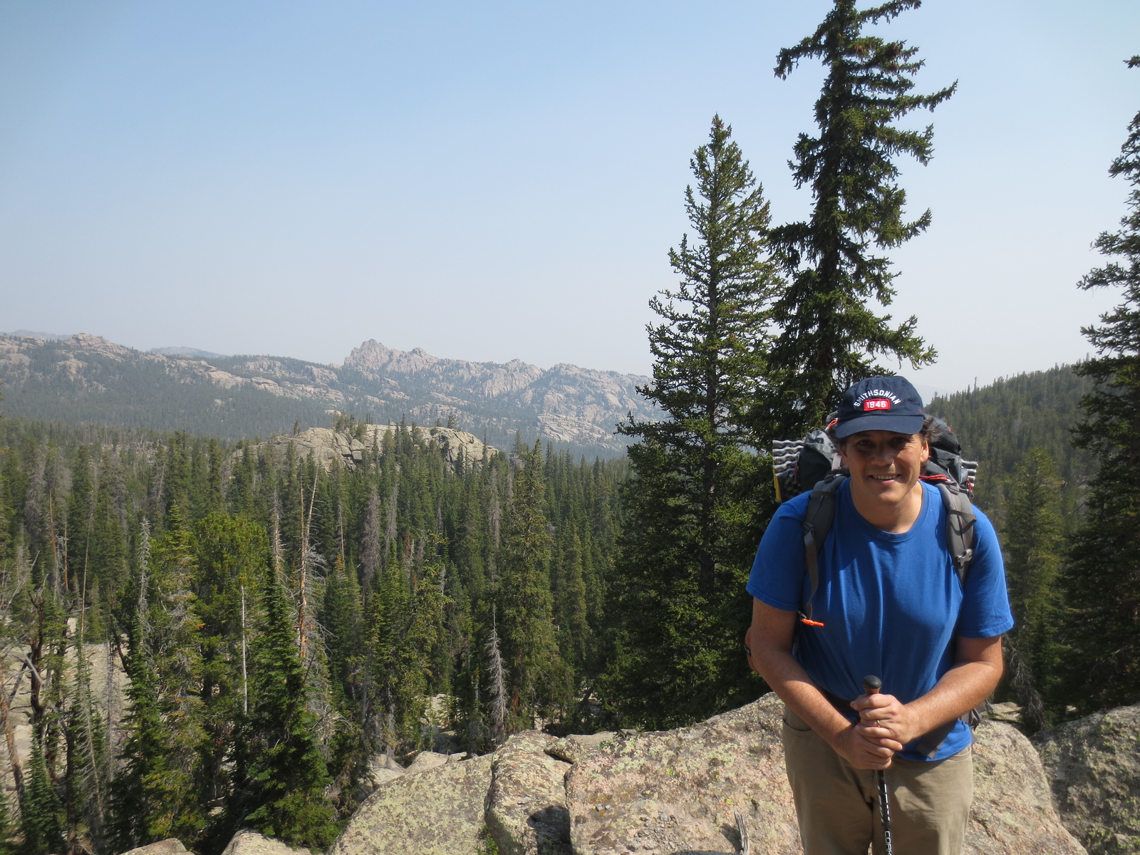 A hiker with a backpack pausing on a forested ridge, mountains behind