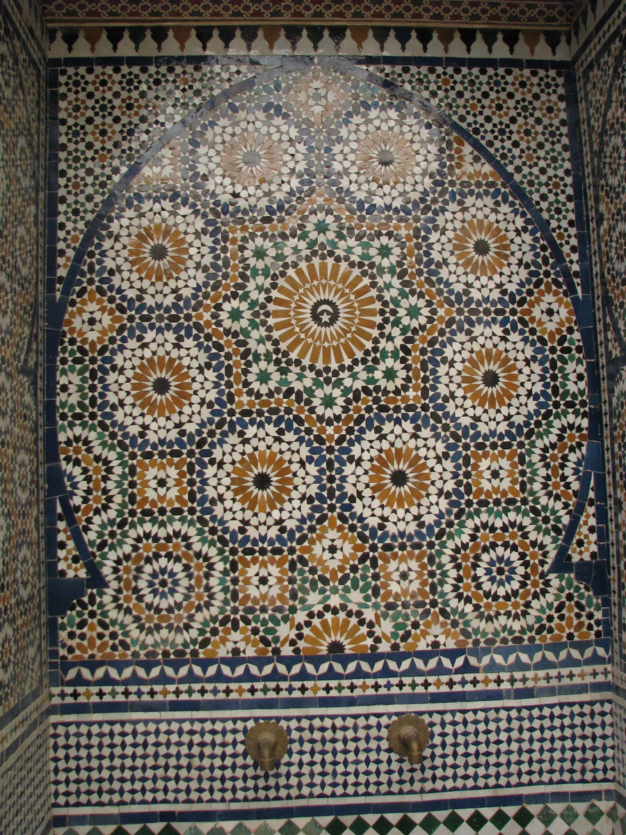 An arched fountain niche covered in intricate Moroccan zellij tilework of interlocking stars and rosettes